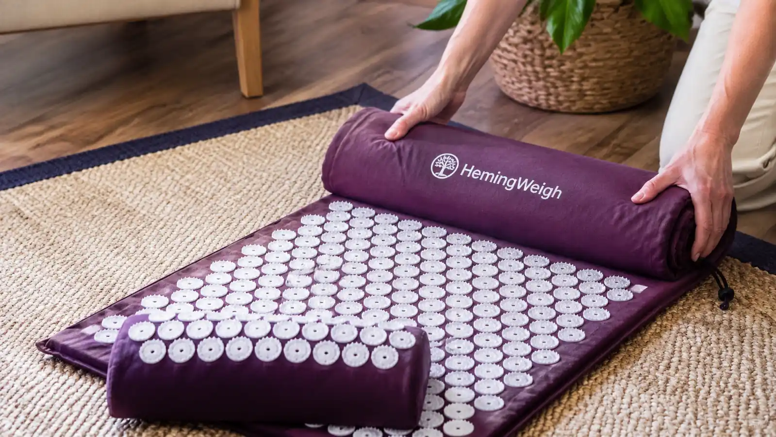 Close-up of hands unrolling the HemingWeigh acupressure mat and pillow set from its carrying bag onto the floor