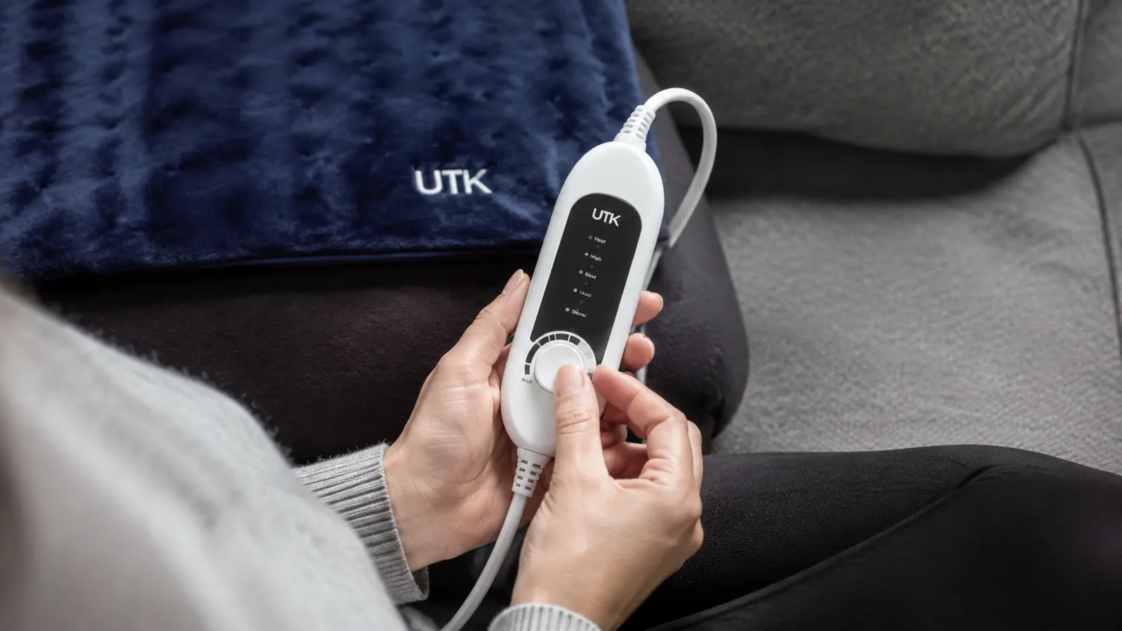 Close-up of a hand adjusting the temperature dial on the UTK infrared heating pad control unit