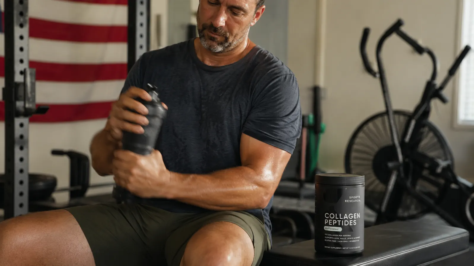 Man mixing a post-workout shaker bottle with collagen and whey protein powder in a home gym