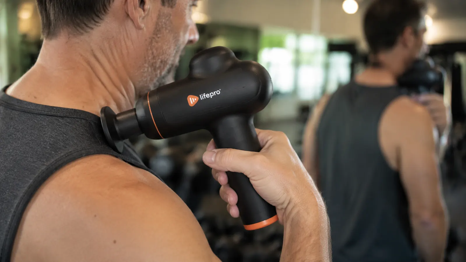 Hand holding the Lifepro massage gun with the flat head attached against a shoulder