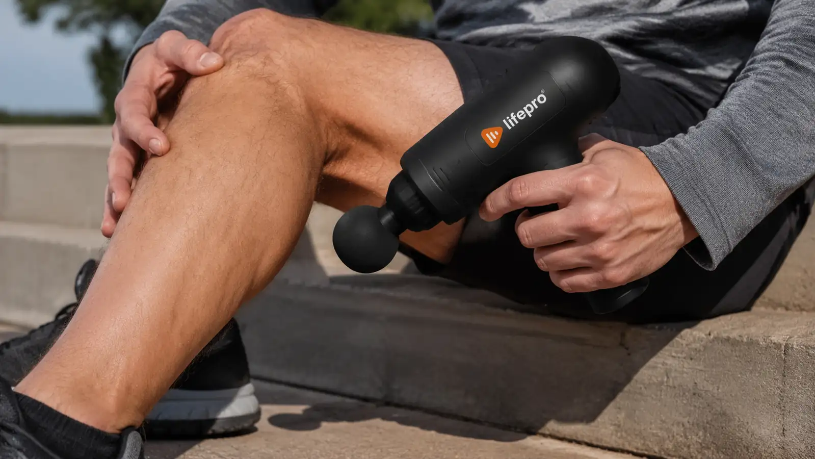 Hand holding the Lifepro massage gun against a calf muscle after a run