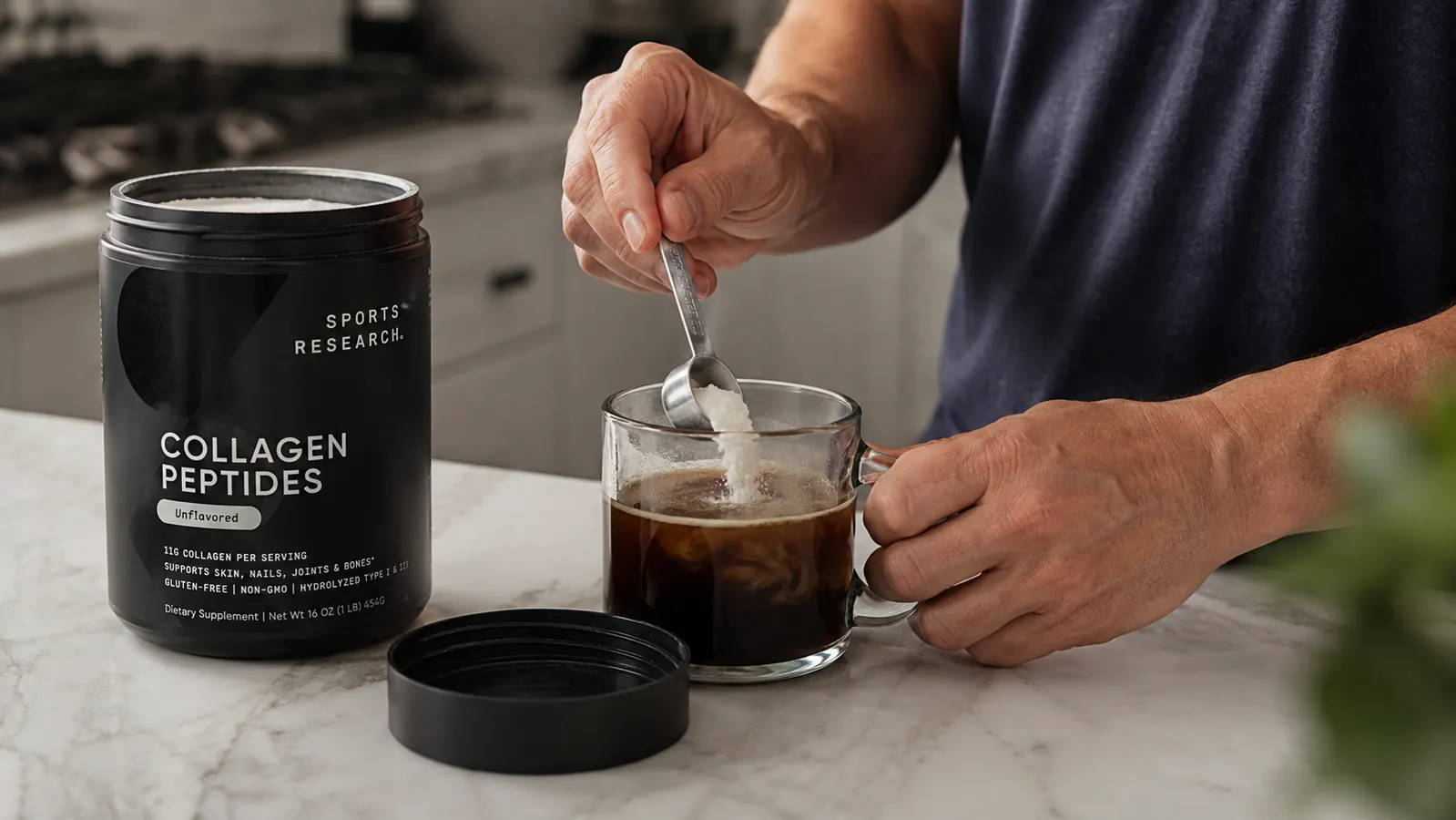 Hand stirring a scoop of collagen powder into a mug of coffee on a kitchen counter