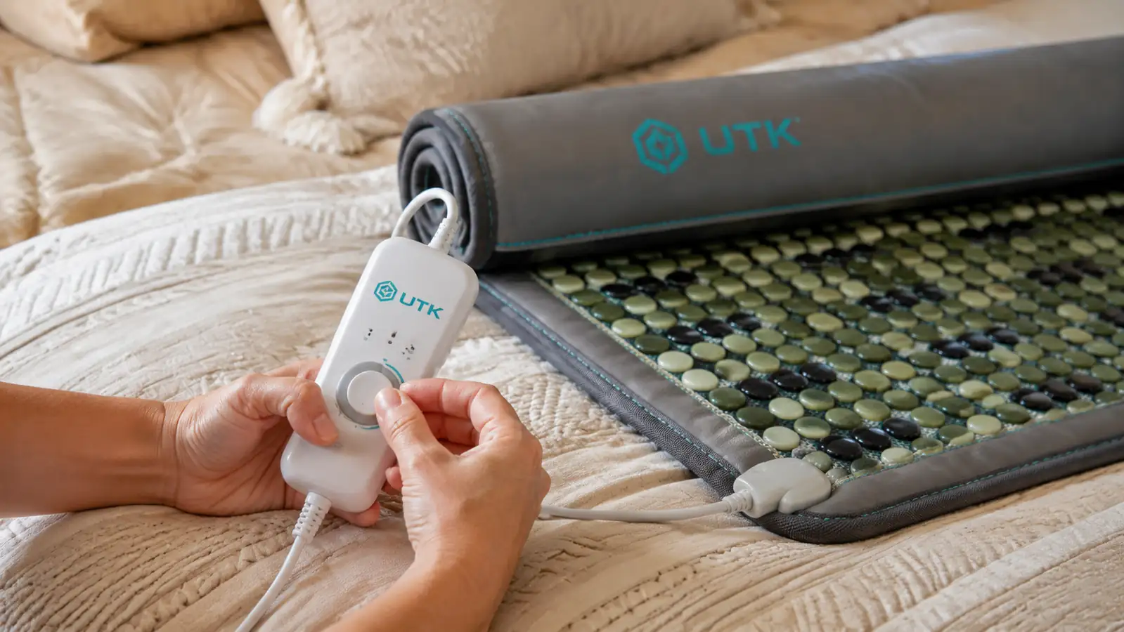 Hand adjusting the temperature dial on the UTK far infrared heating pad controller while the pad sits folded on a bed